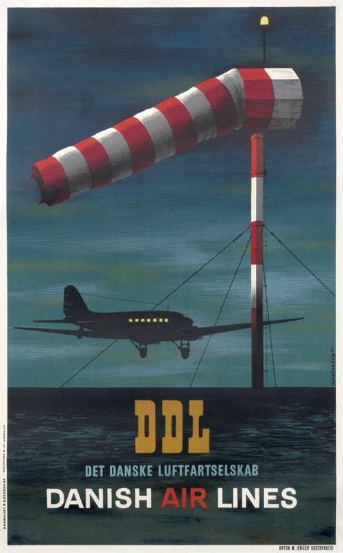 Plane flies close to water at night, beacon flag in foreground; blue, black, red, white