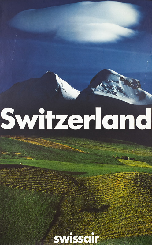 View of Alps with fields and farmers working below; green, yellow, blue, white