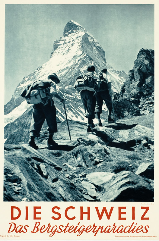 Rear-view photograph of three hikers ascending slope, Matterhorn (Zermatt) in distance; black, white, red
