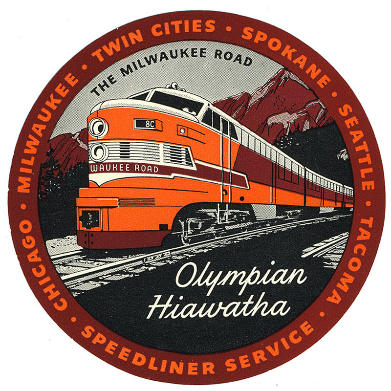 Train running down tracks, mountains behind; purple, orange, black, white