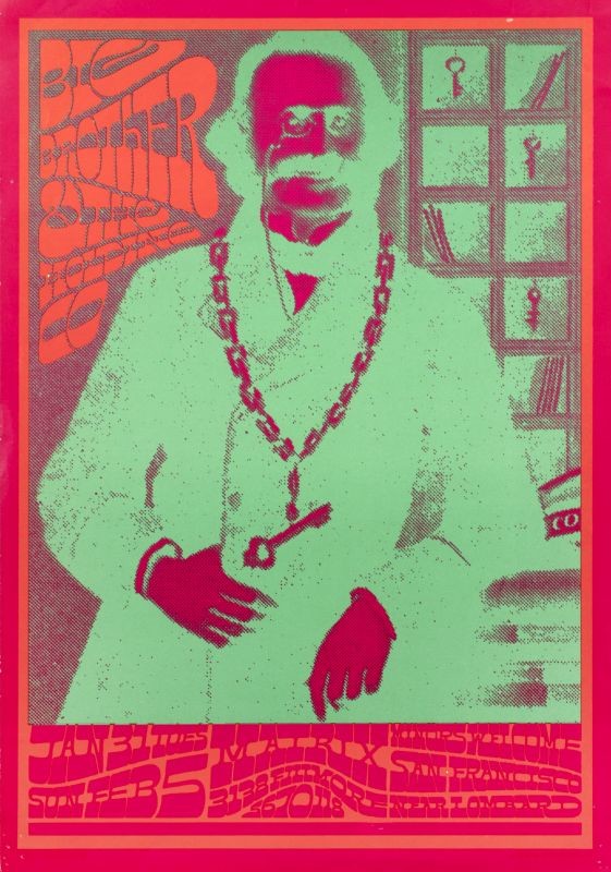 Man with glasses and key around neck sits in front of bookshelf flled with keys; pink, green, orange, neon